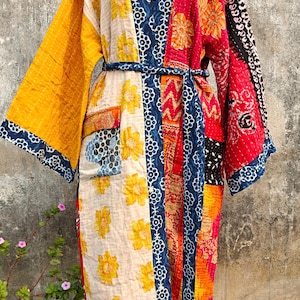 May include: A patchwork robe with a floral and geometric pattern. The robe features a mix of colors including yellow, blue, red, and white. It has long sleeves and a matching belt. The robe is displayed on a mannequin.