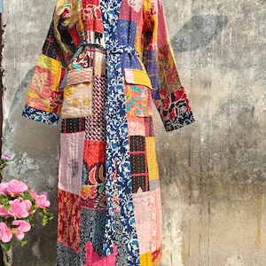Könnte beinhalten: Langer Patchwork-Bademantel mit Wickelgürtel. Er hat bunte Stoffquadrate in Rot, Blau, Gelb und Rosa. Der Bademantel wird auf einer Schaufensterpuppe vor neutralem Hintergrund präsentiert.