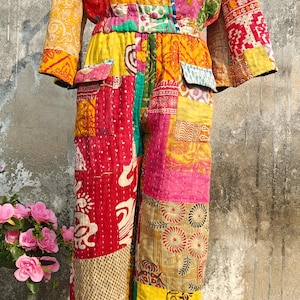 Può includere: Tuta patchwork dai colori vivaci, tra cui giallo, rosso e rosa. L'indumento presenta un top a portafoglio, maniche lunghe e pantaloni a gamba larga. Il tessuto sembra trapuntato con vari motivi.