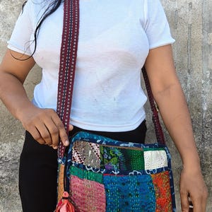 Op de afbeelding: Een vierkante schoudertas met een patchworkontwerp van diverse kleurrijke stofresten in tinten roze, blauw, groen en oranje, geaccentueerd met gedetailleerd kantha-stiksel en een klein stoffen kwastje aan de ritssluiting aan de zijkant.
