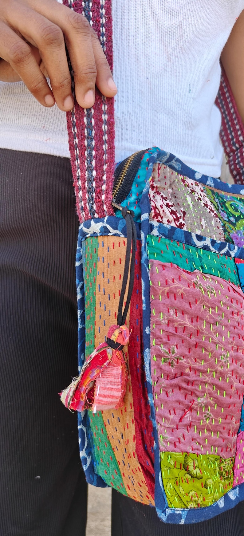 Pode incluir: Uma bolsa de ombro de patchwork com uma variedade de quadrados de tecido coloridos em tons de rosa, verde, azul e laranja. A bolsa &eacute; constru&iacute;da com costuras vis&iacute;veis em estilo kantha e inclui uma al&ccedil;a grossa tecida em bord&ocirc; e branco.