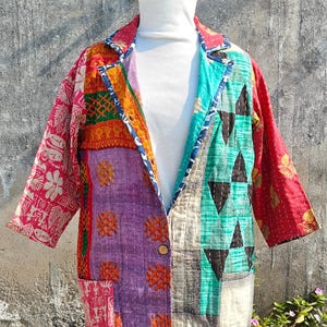 Puede incluir: Blazer patchwork con una variedad de patrones de tela coloridos. La chaqueta presenta una mezcla de diseños florales, geométricos y abstractos en tonos de rojo, morado, verde y naranja. Tiene un cierre de un solo botón y una camisa de cuello alto blanca debajo.