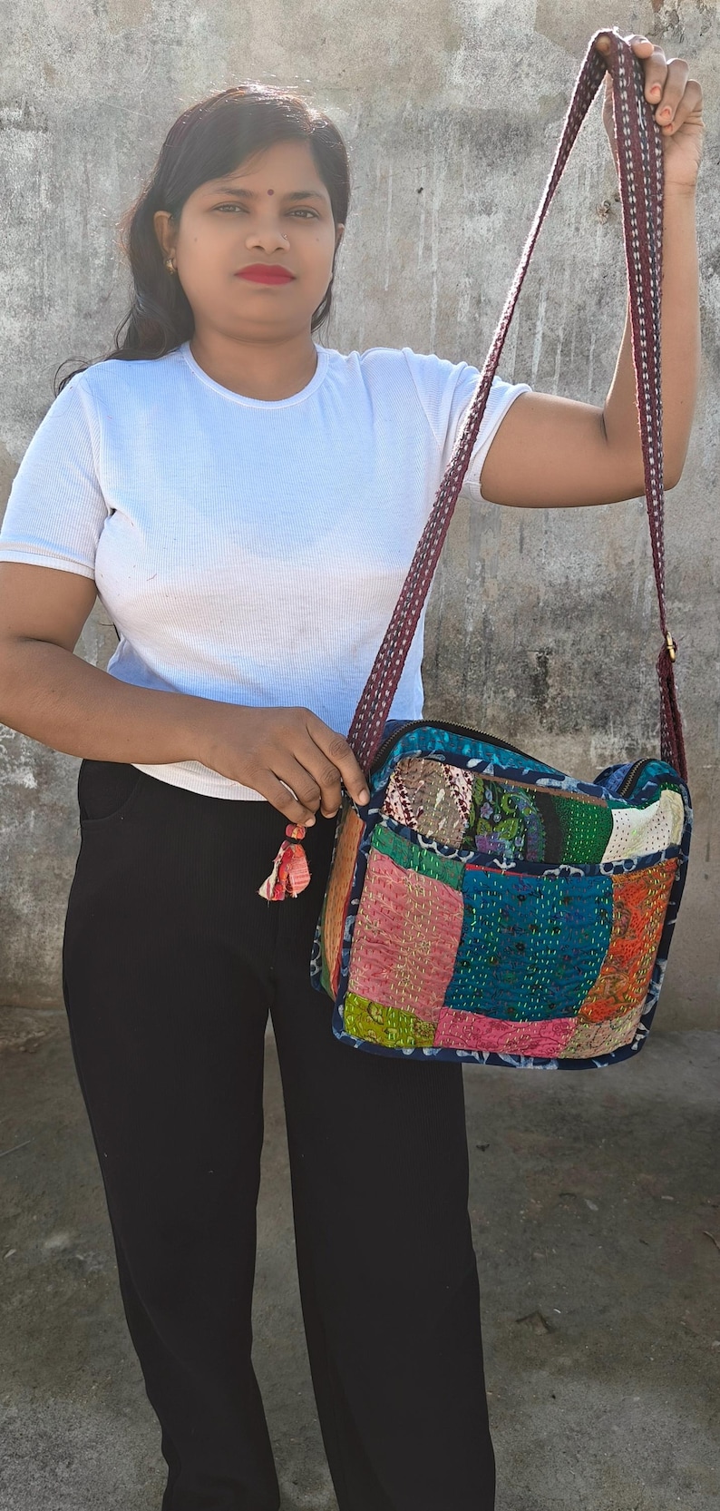 Pode incluir: Uma bolsa tiracolo retangular com um design de patchwork feito de v&aacute;rios quadrados de tecido coloridos em tons de rosa, azul, verde e laranja. A bolsa tem uma al&ccedil;a de ombro longa com padr&atilde;o escuro e uma pequena borla de tecido no z&iacute;per.