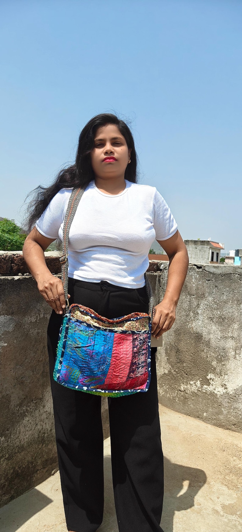 Pode incluir: Uma bolsa tiracolo retangular com um design de patchwork de pain&eacute;is de tecido de cores vibrantes em tons de azul, vermelho e amarelo. A bolsa possui uma al&ccedil;a cinza larga e texturizada, e um fecho de correr superior com costuras vis&iacute;veis.
