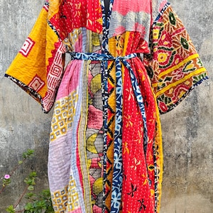 Può includere: Un abito kimono patchwork dai colori vivaci, tra cui rosso, giallo, rosa e blu. L'abito presenta una varietà di motivi geometrici e floreali, con una cintura blu abbinata. L'abito è esposto su un manichino.