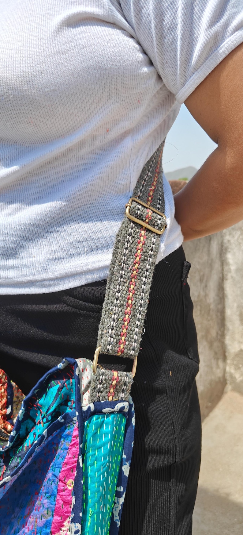 Pode incluir: Uma al&ccedil;a de bolsa transversal feita de tecido cinza com finas listras verticais vermelhas e amarelas, apresentando um ajustador de metal em tom de lat&atilde;o e um conector em D preso a uma bolsa de tecido acolchoado multicolorido com costuras verdes.