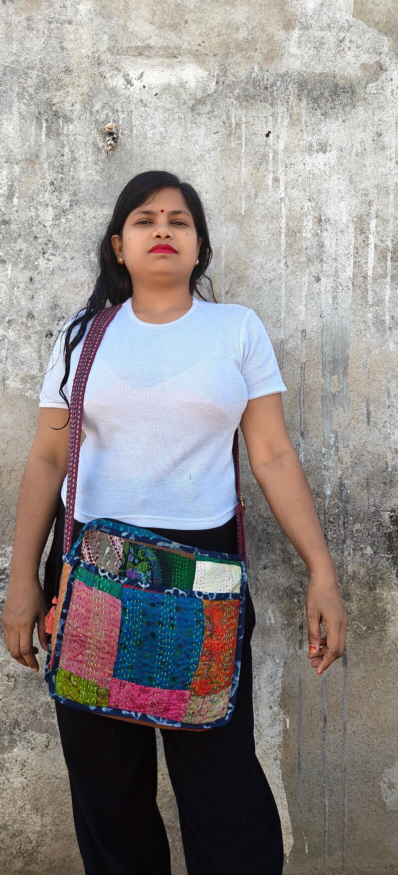 Pode incluir: Uma bolsa tiracolo retangular com um design de patchwork feito de v&aacute;rios quadrados de tecido coloridos com costuras kantha complexas. A bolsa tem uma al&ccedil;a longa estampada e &eacute; usada sobre uma camiseta branca e cal&ccedil;as pretas.