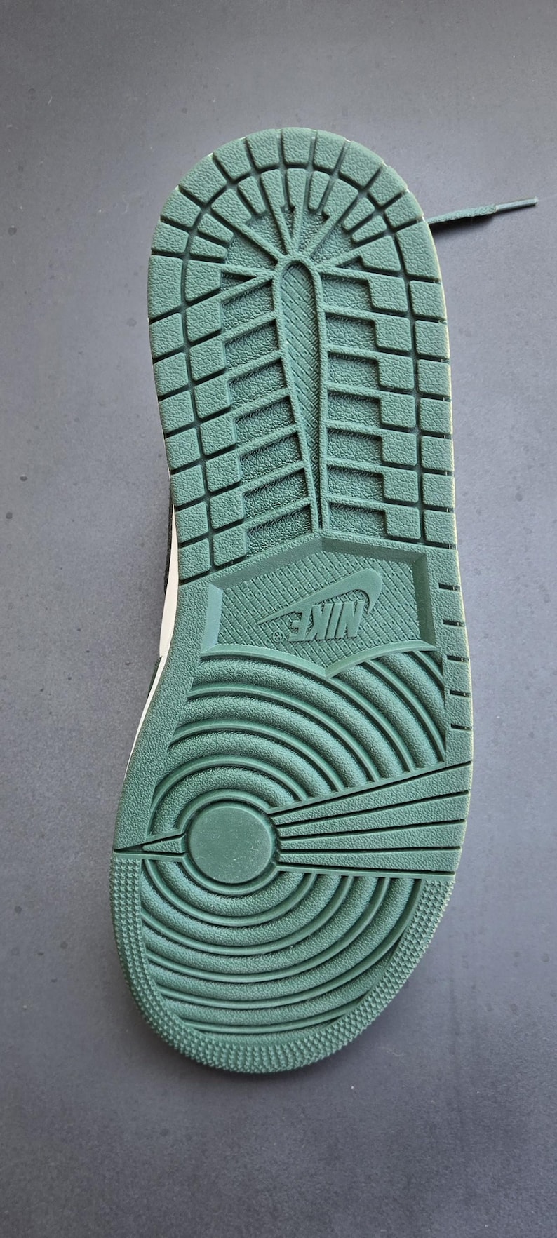 Puede incluir: Primer plano de la suela de una zapatilla deportiva verde y blanca. La suela est&aacute; texturizada con una variedad de patrones, incluido un logotipo de Nike, ranuras y un dise&ntilde;o circular. El zapato est&aacute; dise&ntilde;ado para la tracci&oacute;n y el agarre.