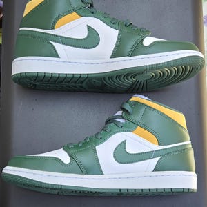 Puede incluir: Par de zapatillas altas verdes, blancas y amarillas. Las zapatillas presentan un logotipo de Nike blanco en el lateral, una entresuela blanca y una suela verde. La parte superior es verde con detalles amarillos.