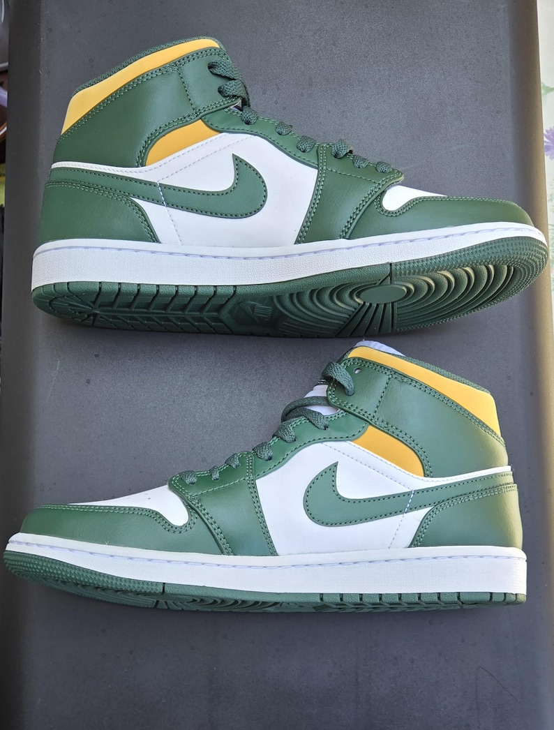 Puede incluir: Par de zapatillas altas verdes, blancas y amarillas. Las zapatillas presentan un logotipo de Nike blanco en el lateral, una entresuela blanca y una suela verde. La parte superior es verde con detalles amarillos.