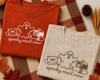 Puede incluir: Una camiseta color óxido y una camiseta beige, cada una con un gráfico blanco o marrón oscuro de un fantasma, un sobre con un corazón y un buzón, con el texto "spooky mail crew" impreso en fuente cursiva debajo del diseño gráfico.