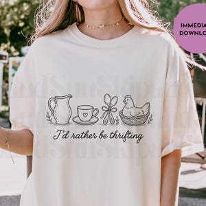 May include: Cream-colored t-shirt with a black line drawing of a pitcher, teacup, scissors, and a hen in a basket. The text "I'd rather be thrifting" is below the illustrations. A purple circle with "IMMEDIATE DOWNLOAD" is in the upper right.
