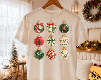 Puede incluir: Una camiseta de manga corta de color crema con un estampado gráfico de nueve adornos navideños distintos dispuestos en una cuadrícula de tres por tres. Los adornos muestran varios patrones festivos que incluyen rayas rojas y verdes, lazos, copos de nieve y acebo.