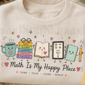 May include: A cream-colored sweatshirt featuring a graphic of a smiling coffee mug, a stack of books labeled Math, Algebra, Geometry, Statistics, and Calculus, an open book, a tablet with the text Let's Solve It, a notebook, and a pencil. The text reads Math Is My Happy Place, Think, Solve, Learn, Repeat.
