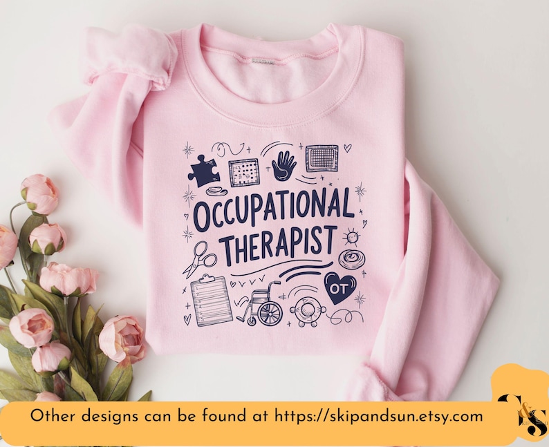 Puede incluir: Sudadera rosa con el texto "Occupational Therapist" en letras azul marino. El dise&ntilde;o incluye varios iconos relacionados con la terapia ocupacional, como una pieza de rompecabezas, una mano, una silla de ruedas y un estetoscopio.