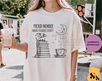 May include: Cream-colored t-shirt with a graphic design featuring a dragon atop a stack of books, a crescent moon, and a teacup. The text reads "PROUD MEMBER FANTASY READERS SOCIETY." A purple circle with the words "IMMEDIATE DOWNLOAD" is on the right.