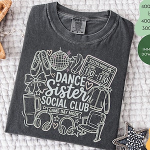 May include: Dark grey t-shirt with a white graphic design featuring ballet shoes, a disco ball, and the text "DANCE Sister SOCIAL CLUB GAME DAY MODE". The shirt also includes a score board that reads "10-10".