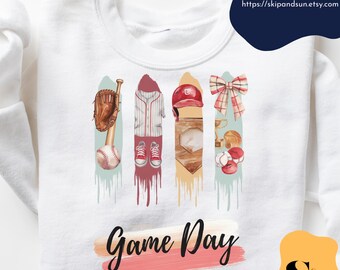 May include: White sweatshirt with a watercolor design of baseball equipment, including a bat, glove, ball, jersey, cap, and trophy. The text "Game Day" is written in pink and red on the sweatshirt.