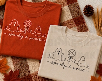 Puede incluir: Dos camisetas, una de color naranja óxido y otra crema, cada una con un dibujo de línea continua de un fantasma, una piruleta y un caramelo de maíz. Debajo de las ilustraciones, el texto "spooky & sweet" está escrito en letra cursiva.