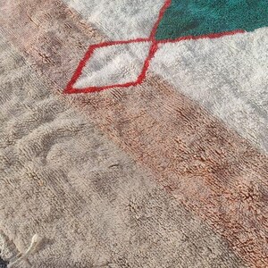 May include: A white, beige, and green rug with a geometric pattern. The rug has a fringe border and is made of a soft, fluffy material.