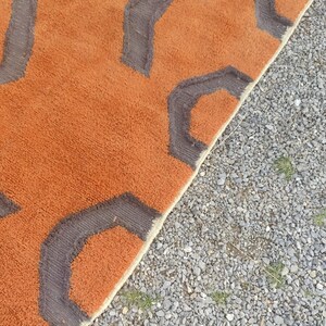 May include: A close-up of a brown and gray rug with a geometric pattern. The rug has a fringe border and is made of a soft, plush material.