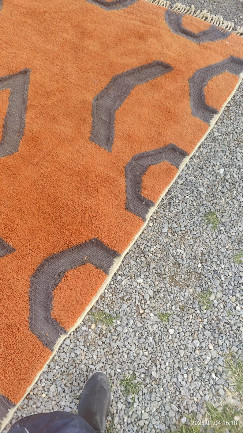 May include: A close-up of a brown and gray rug with a geometric pattern. The rug has a fringe border and is made of a soft, plush material.
