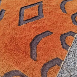 May include: A large, orange and brown rug with a geometric pattern. The rug has a fringe border and is made of a soft, plush material.