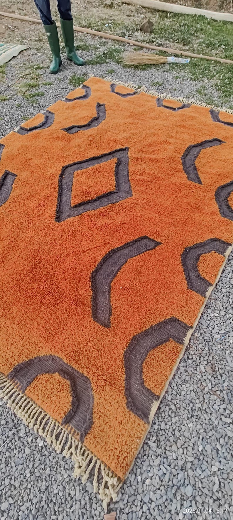 May include: A large, orange and brown rug with a geometric pattern. The rug has a fringe border and is made of a soft, plush material.