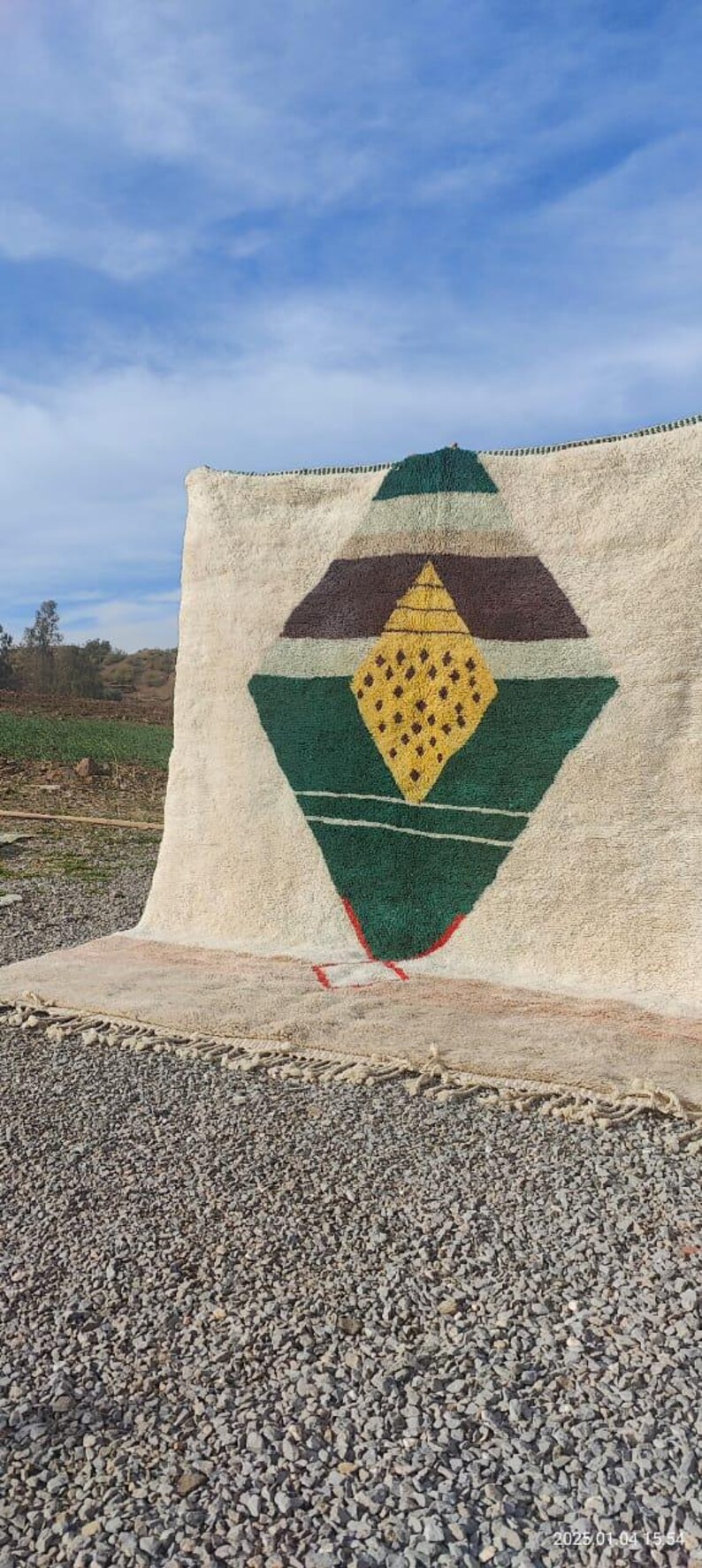 May include: A white rug with a green, brown, and yellow geometric design. The rug has a fringe border.
