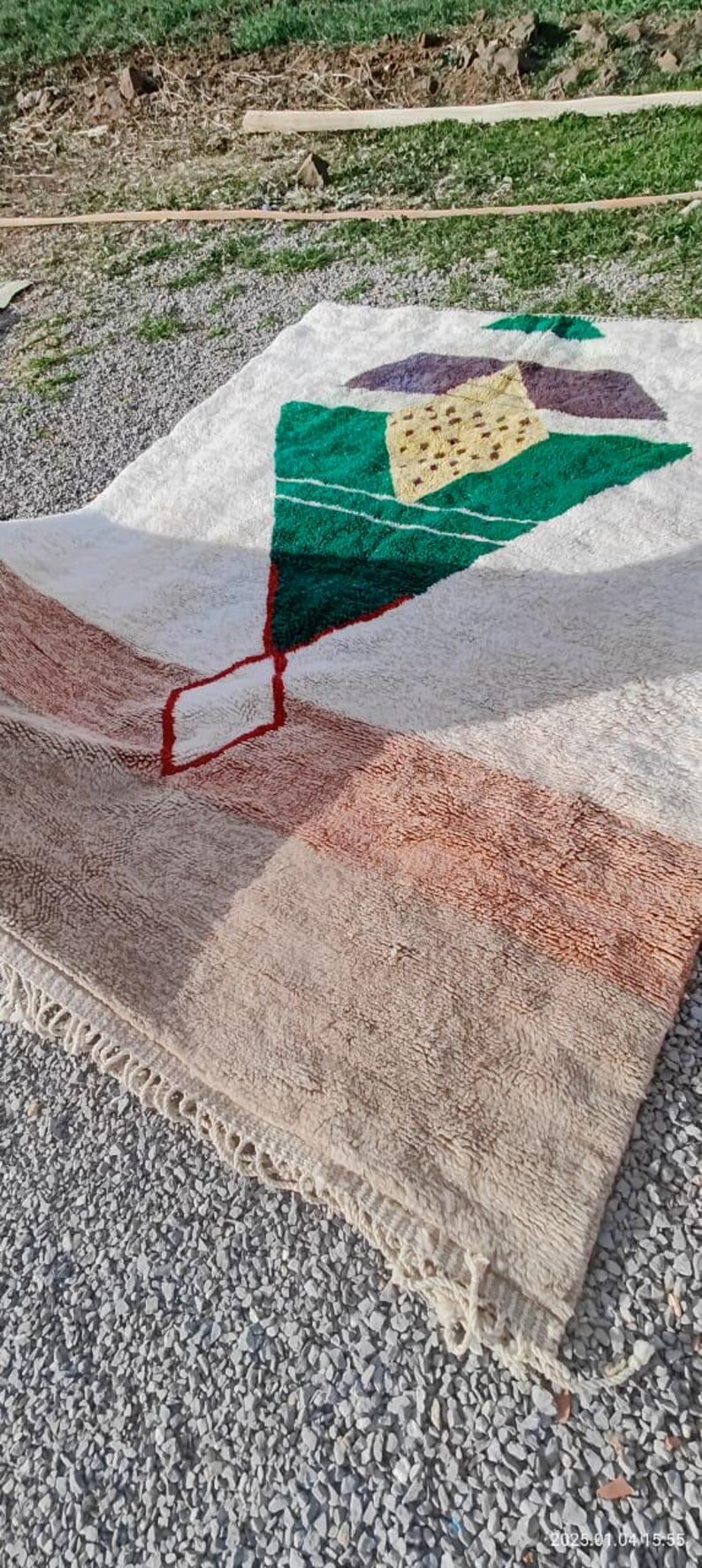 May include: A white, beige, green, and red Moroccan rug with a geometric design. The rug has a fringe border.