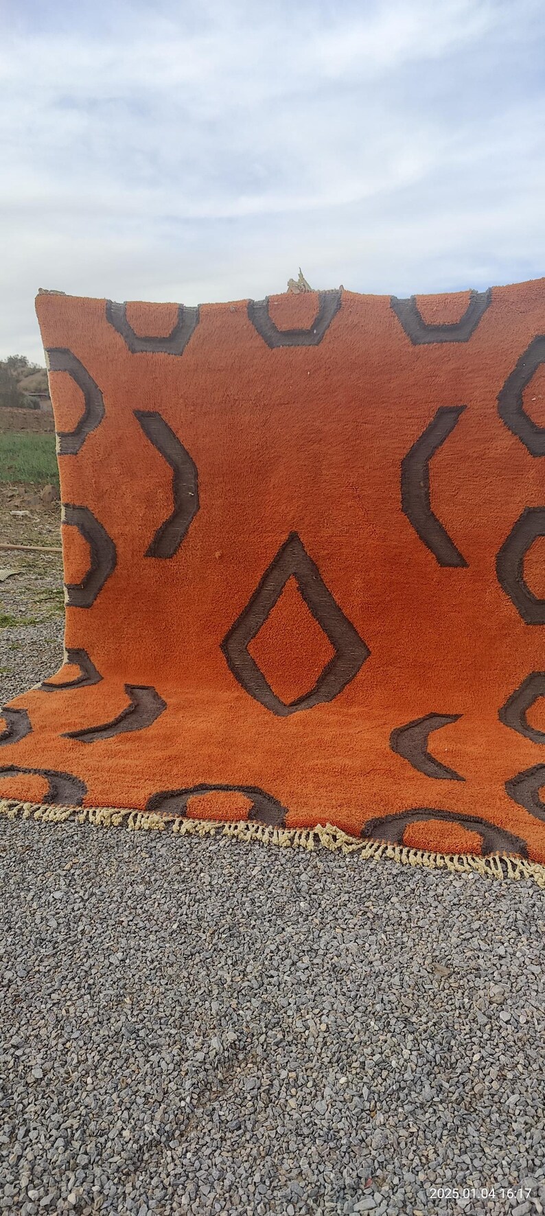May include: A large, orange rug with a geometric pattern in brown. The rug has a fringe border.