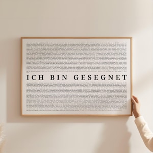 Könnte beinhalten: Ein gerahmter Druck mit einem hellen Holzrahmen. Der Druck zeigt einen Hintergrund aus kleinem Text und die Worte "ICH BIN GESEGNET" in großen, fetten, schwarzen Buchstaben. Der Druck wird von einer Hand gehalten.