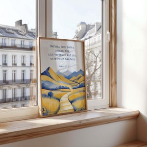 May include: A framed art print featuring a watercolor landscape with a path winding through yellow and blue hills. The print includes the text "Befiehl dem Herrn deinen Weg, und vertraue auf ihn, so wird er handeln. Psalm 37.5."