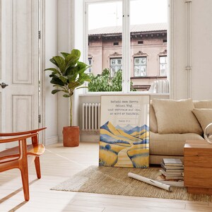 May include: A framed print with a watercolor landscape of yellow and blue mountains and a winding road. The print includes German text from Psalm 37:5. The artwork is displayed on a rug in a living room setting.
