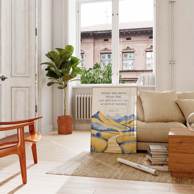 May include: A framed print with a watercolor landscape of yellow and blue mountains and a winding road. The print includes German text from Psalm 37:5. The artwork is displayed on a rug in a living room setting.