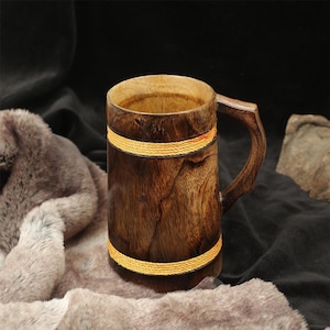 May include: A dark brown wooden mug featuring a cylindrical body with visible wood grain patterns, a sturdy handle, and two horizontal bands of bright yellow rope wrapped around the upper and lower sections of the exterior surface.