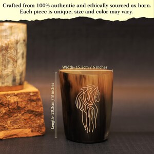 May include: An ox horn drinking cup with a horse design etched on the side. The cup is 20.3cm tall and 15.2cm wide. The horn has a natural colour gradient from light brown to black.