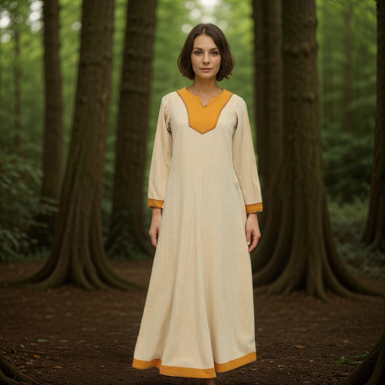 May include: A long, white dress with a yellow neckline and trim. The dress is worn by a person standing in a forest.