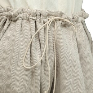 May include: A pair of beige pants with a herringbone pattern and a drawstring waist.