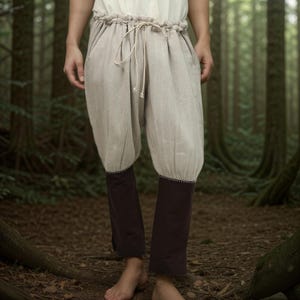May include: A pair of beige linen pants with a drawstring waist and dark brown fabric at the bottom of the legs.