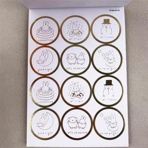 May include: A sheet of white stickers with gold foil borders. Each sticker features a black and white illustration of a bunny or snowman with phrases like "summertime", "let it rain", and "shine bright".