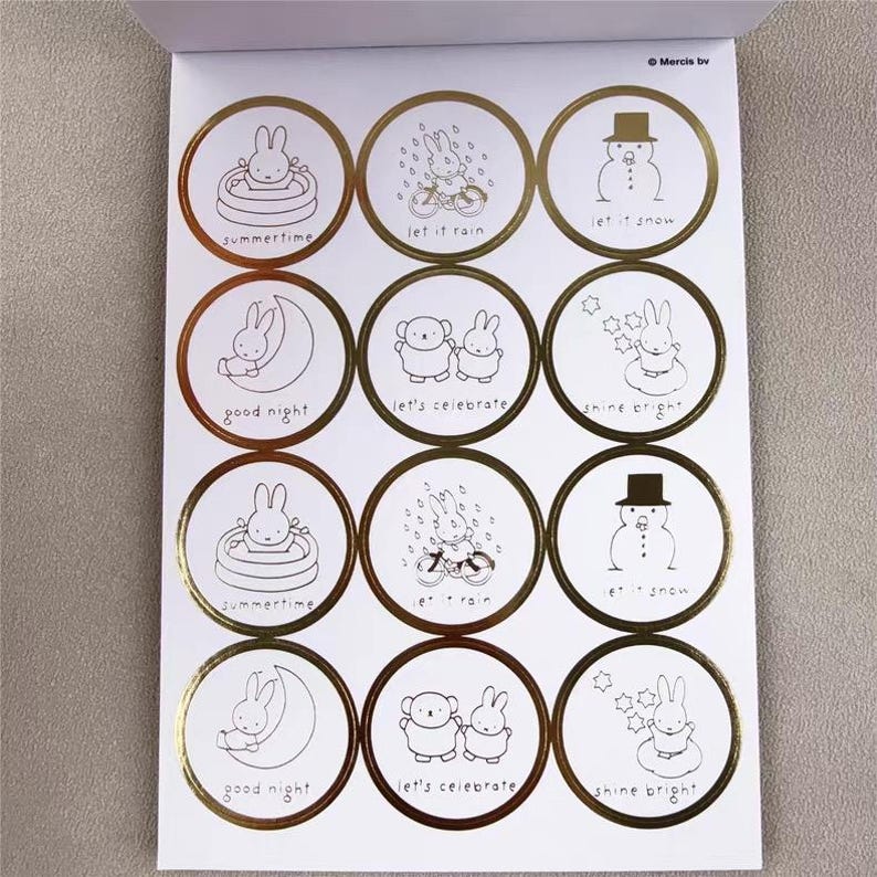 May include: A sheet of white stickers with gold foil borders. Each sticker features a black and white illustration of a bunny or snowman with phrases like "summertime", "let it rain", and "shine bright".