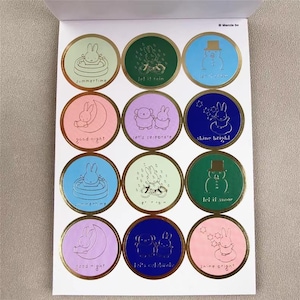 May include: Sheet of round stickers with gold foil edges. Each sticker features a different illustration of a bunny or snowman with phrases like "summertime", "let it rain", and "good night".