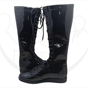 May include: A pair of tall, black, glossy boots with a lace-up design. The boots have a shiny, patent leather-like finish and a flat sole. The laces run up the front of the boots, adding a classic touch to the footwear.