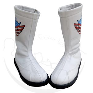Pode incluir: Um par de botas brancas com sola preta. Cada bota apresenta um emblema colorido com um desenho da bandeira americana. As botas são feitas de um material liso e têm uma forma alta e cilíndrica, adequadas para fantasias ou eventos temáticos.