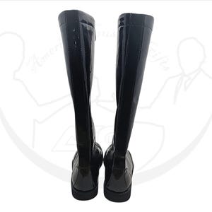 May include: A pair of black knee-high boots with a glossy patent leather finish. The boots have a sleek, streamlined design with a flat sole and a zipper detail on the side. The boots are displayed against a white background.