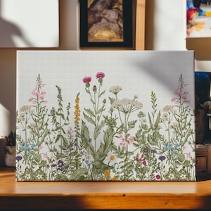 May include: A white canvas print featuring a floral design with a variety of wildflowers in shades of pink, purple, blue, yellow, and green. The flowers are arranged in a horizontal row across the canvas.