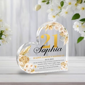 Könnte beinhalten: Ein herzförmiger, transparenter Acryl-Briefbeschwerer mit goldenem Blumendesign und der Zahl 21. Der Text "Sophia, Happy Golden Birthday 20.12.2025" ist auf dem Briefbeschwerer gedruckt. Der Text "On this birthday I hope you always remember how loved, beautiful, strong, creative, worthy, unique and amazing you are. You truly are golden! Love, Mom and Dad and Samantha" ist ebenfalls auf dem Briefbeschwerer gedruckt.
