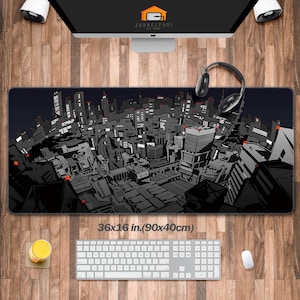 Peut inclure: Un grand tapis de bureau noir et gris avec un motif de paysage urbain détaillé. Le tapis mesure 90x40cm et comprend le texte "36x16 in.(90x40cm)". Un clavier d'ordinateur, une souris et un casque sont sur la surface en bois.
