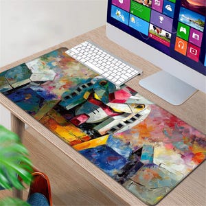 Può includere: Un tappetino per mouse rettangolare con una pittura astratta e colorata di un robot. L'opera d'arte utilizza una tavolozza di blu, gialli, rossi e bianchi. Una tastiera bianca e un monitor del computer sono visibili sullo sfondo. Il tappetino è su una scrivania di legno.